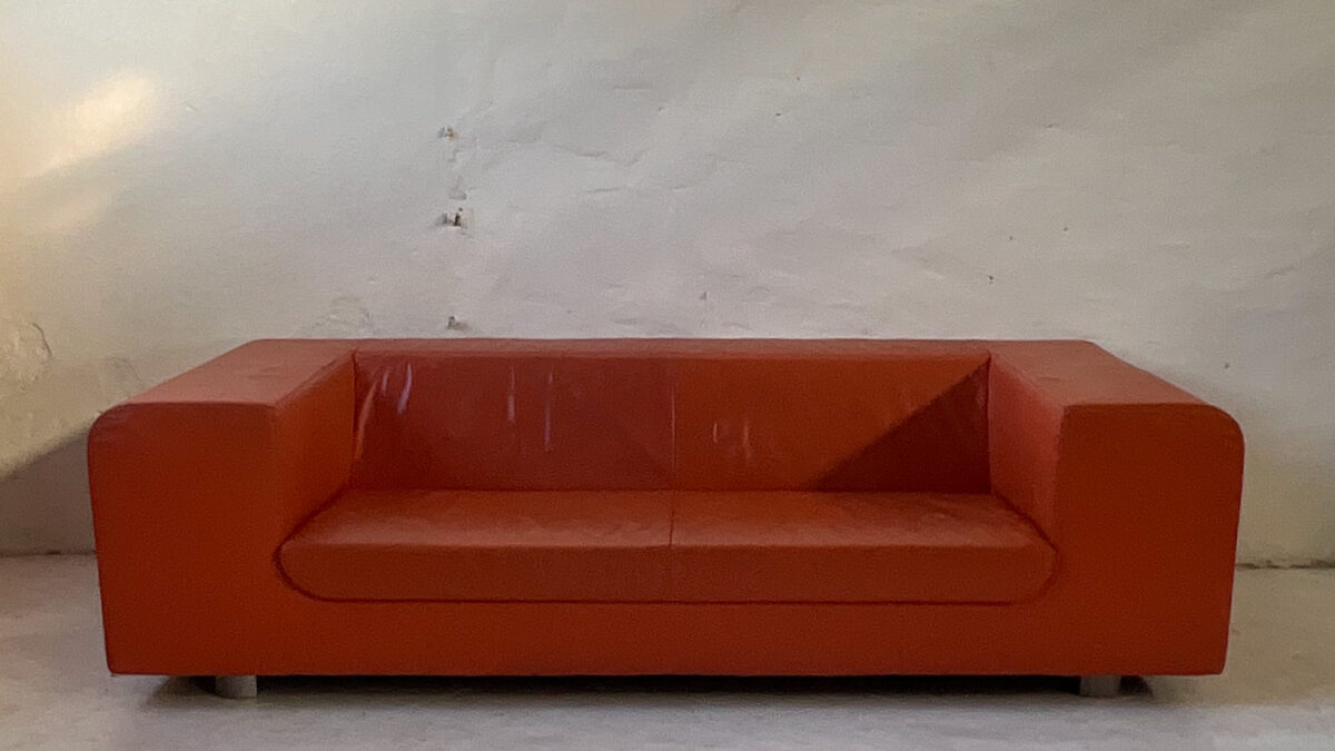 Pomarańczowa skórzana sofa Montis Malou projektu Gijsa Papavoine'a, z szerokimi zaokrąglonymi podłokietnikami.