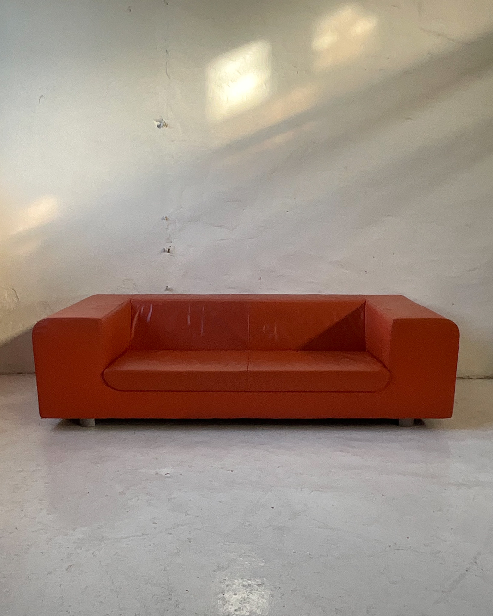 Pomarańczowa skórzana sofa Montis Malou projektu Gijsa Papavoine'a, z szerokimi zaokrąglonymi podłokietnikami.